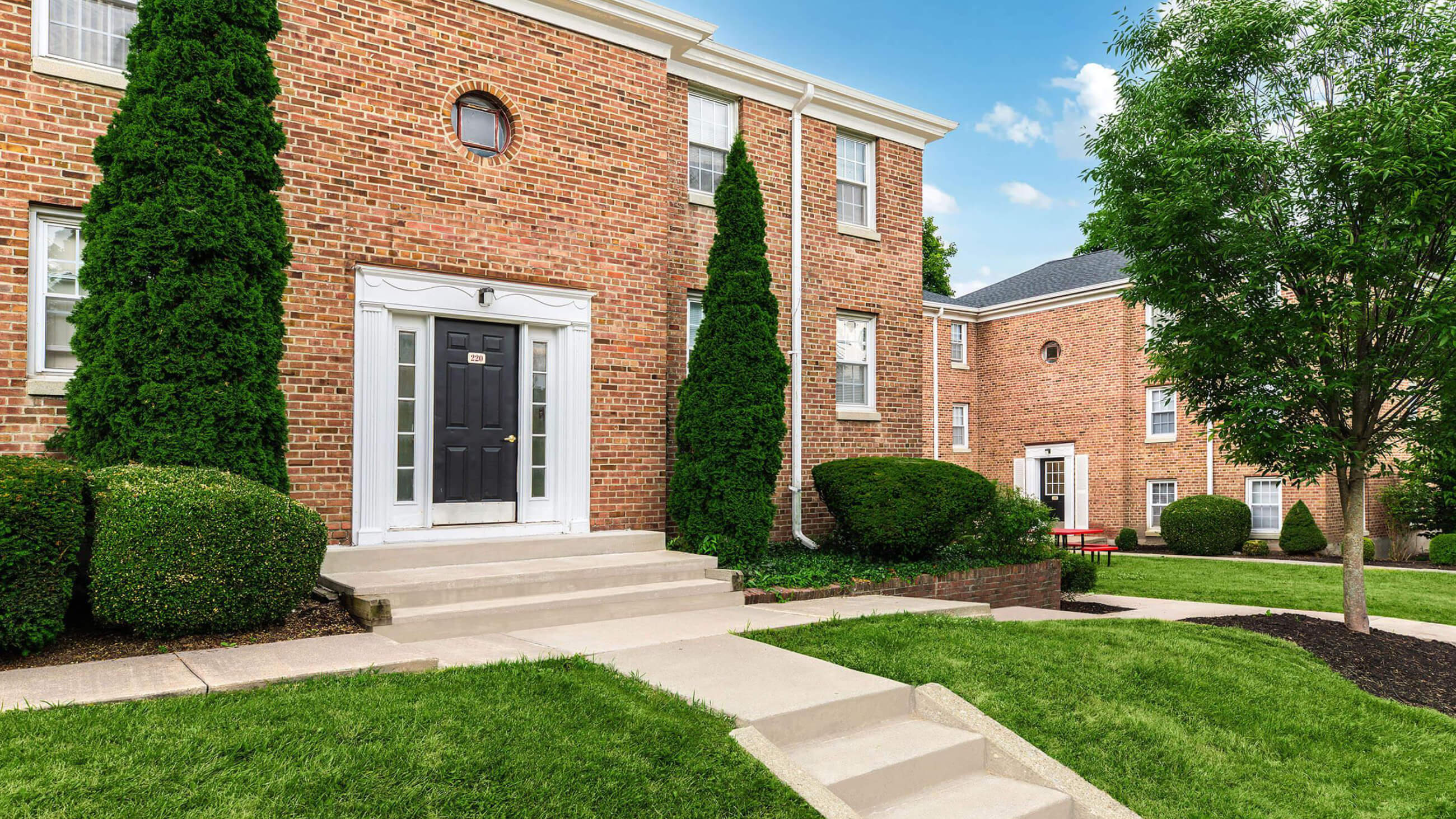 Brick apartment building entrance with landscaped lawn and concrete walkway